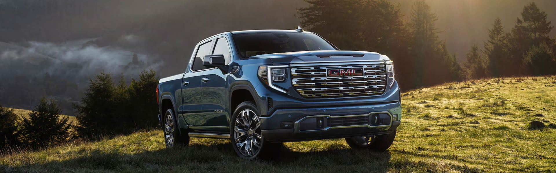 A blue GMC Sierra driving up a grassy hill.